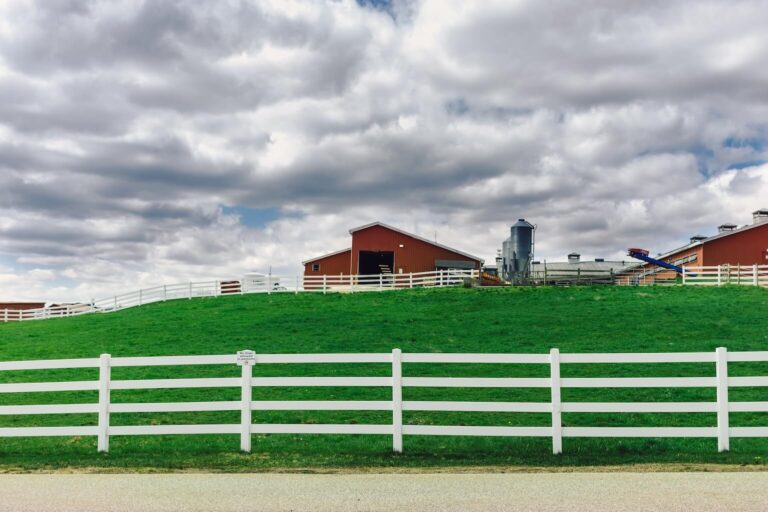a dairy farm with a red barn, surrounded by white three-rail hdpe fencing